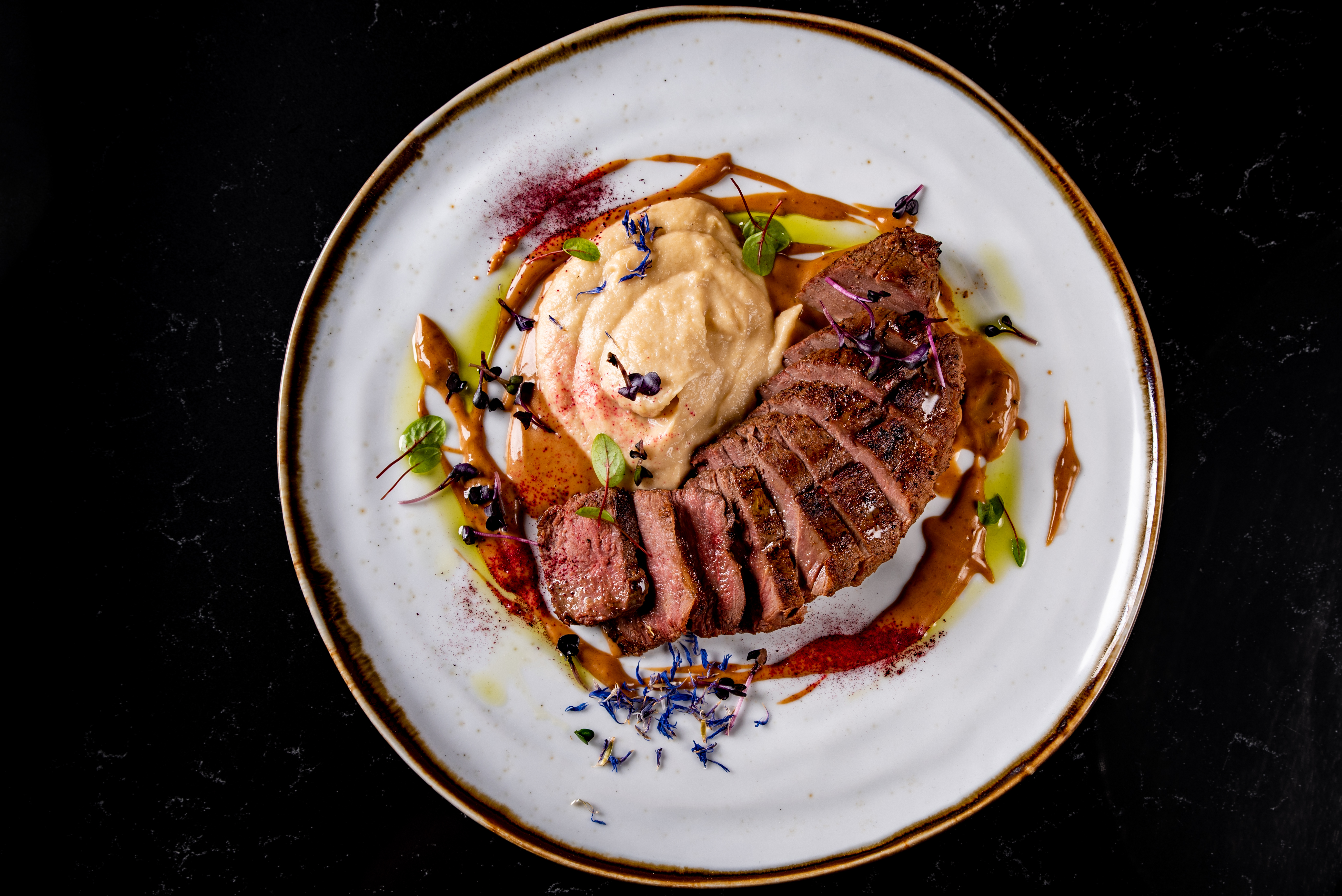 Sliced wild duck breast on a ceramic plate with puree and a dark jus.