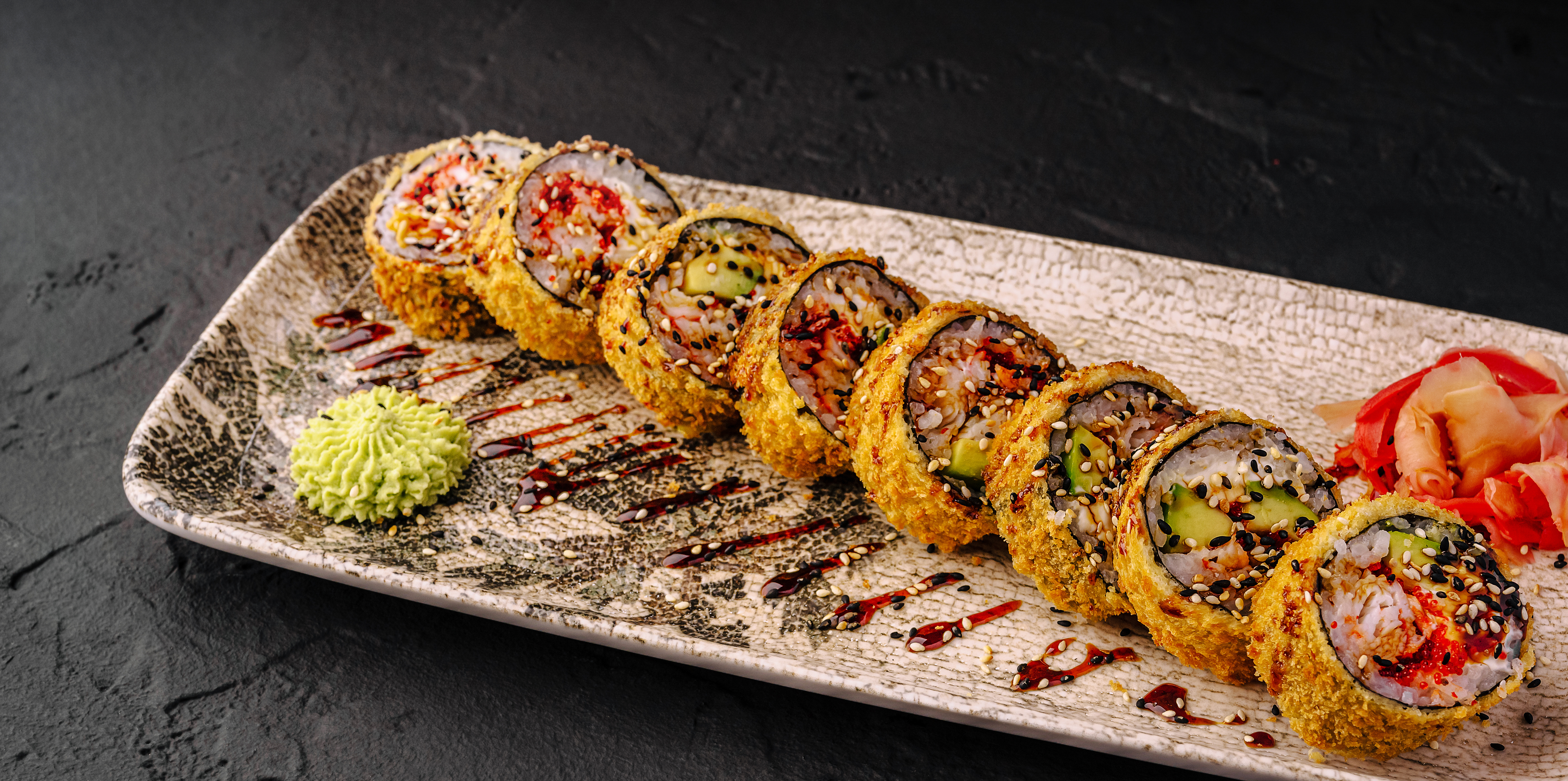 Fried sushi rolls with wasabi and pickled ginger on a ceramic plate.
