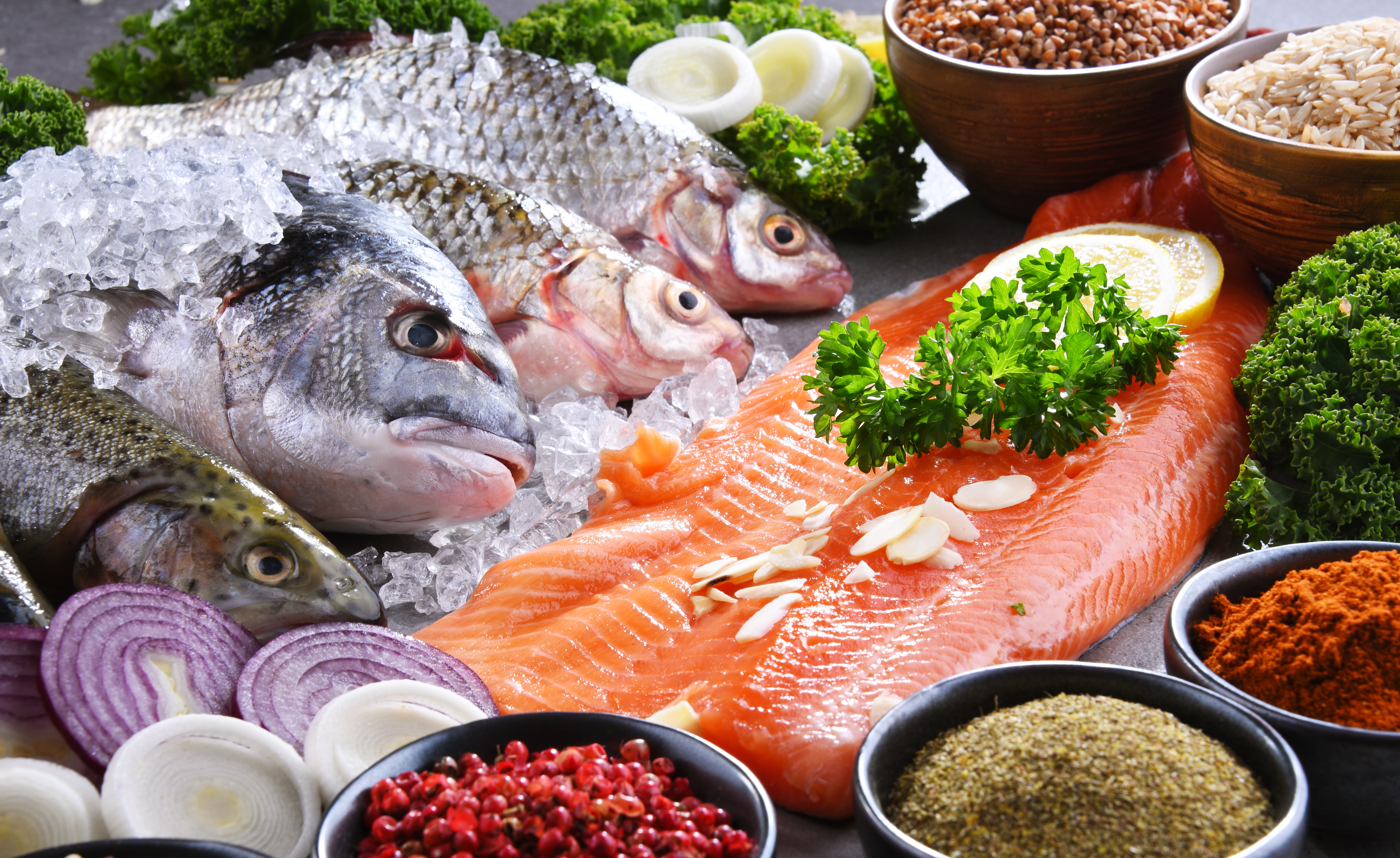 Whole silver fish on crushed ice beside a salmon fillet, lemon, and spices.