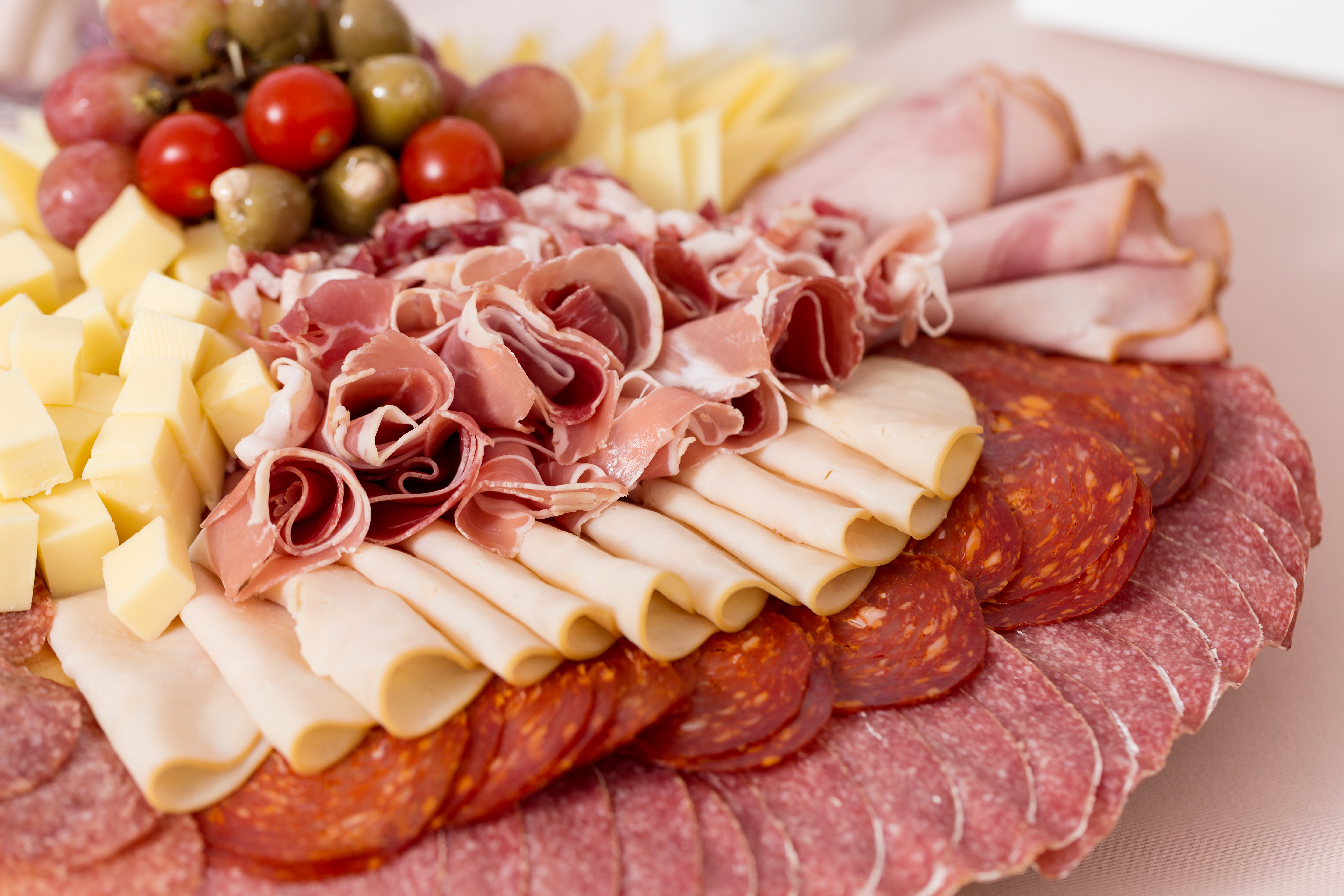 Prosciutto, salami, cubed cheese, olives, and grapes on a crowded board.