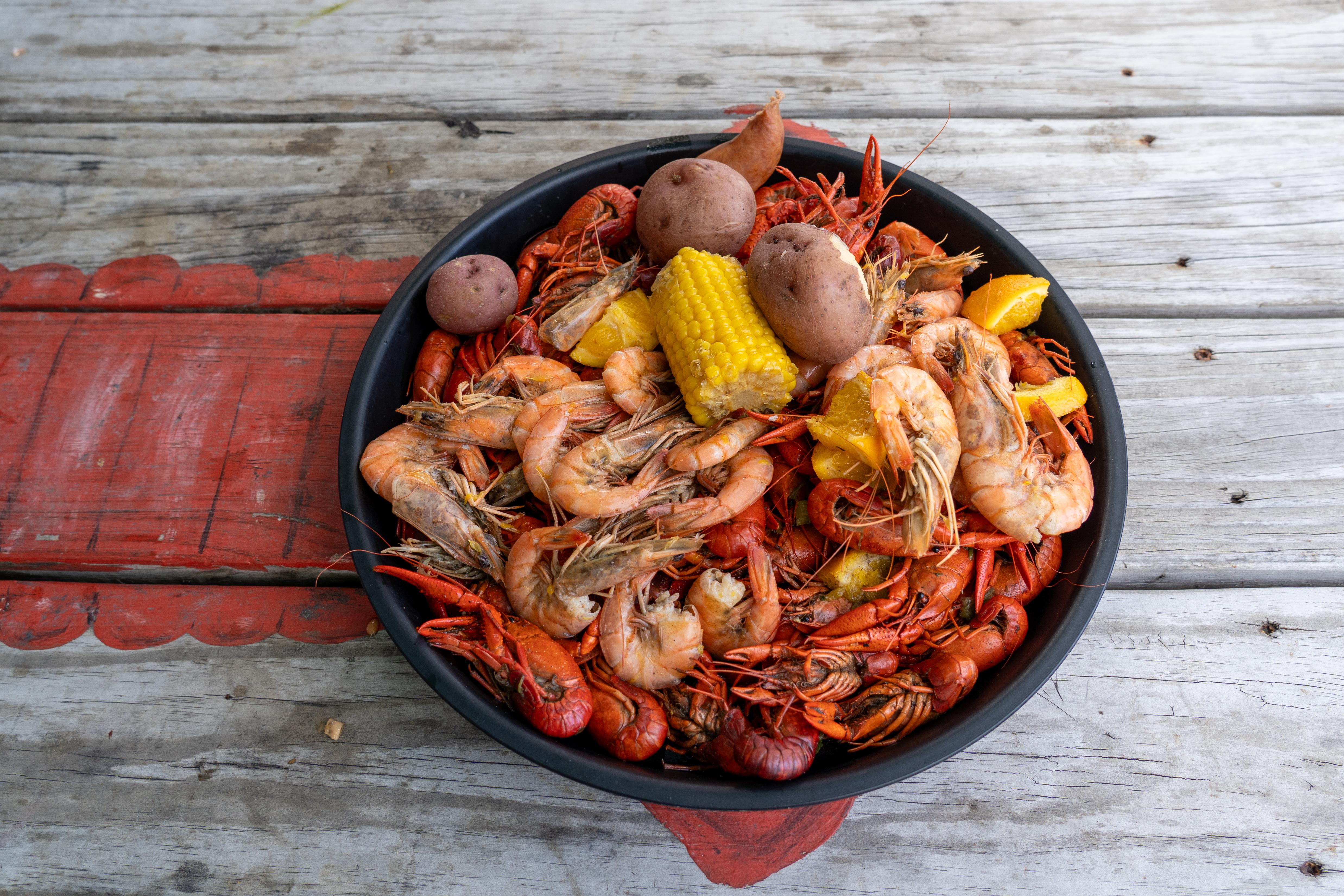 Crawfish and shrimp in a boil with corn, potatoes, and citrus on a rustic table.