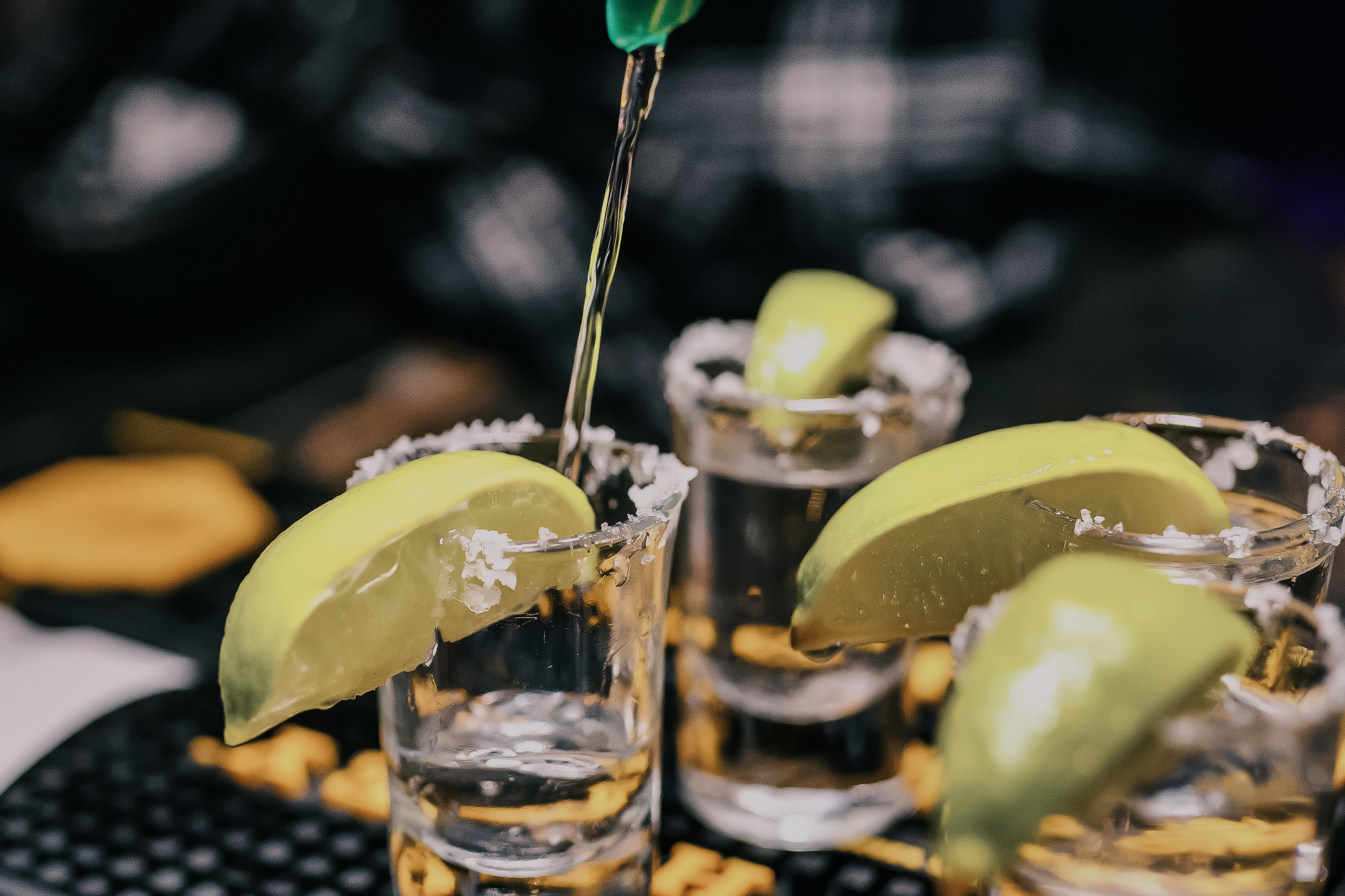 Salt-rimmed shot glasses with lime wedges, a clear spirit poured from above.