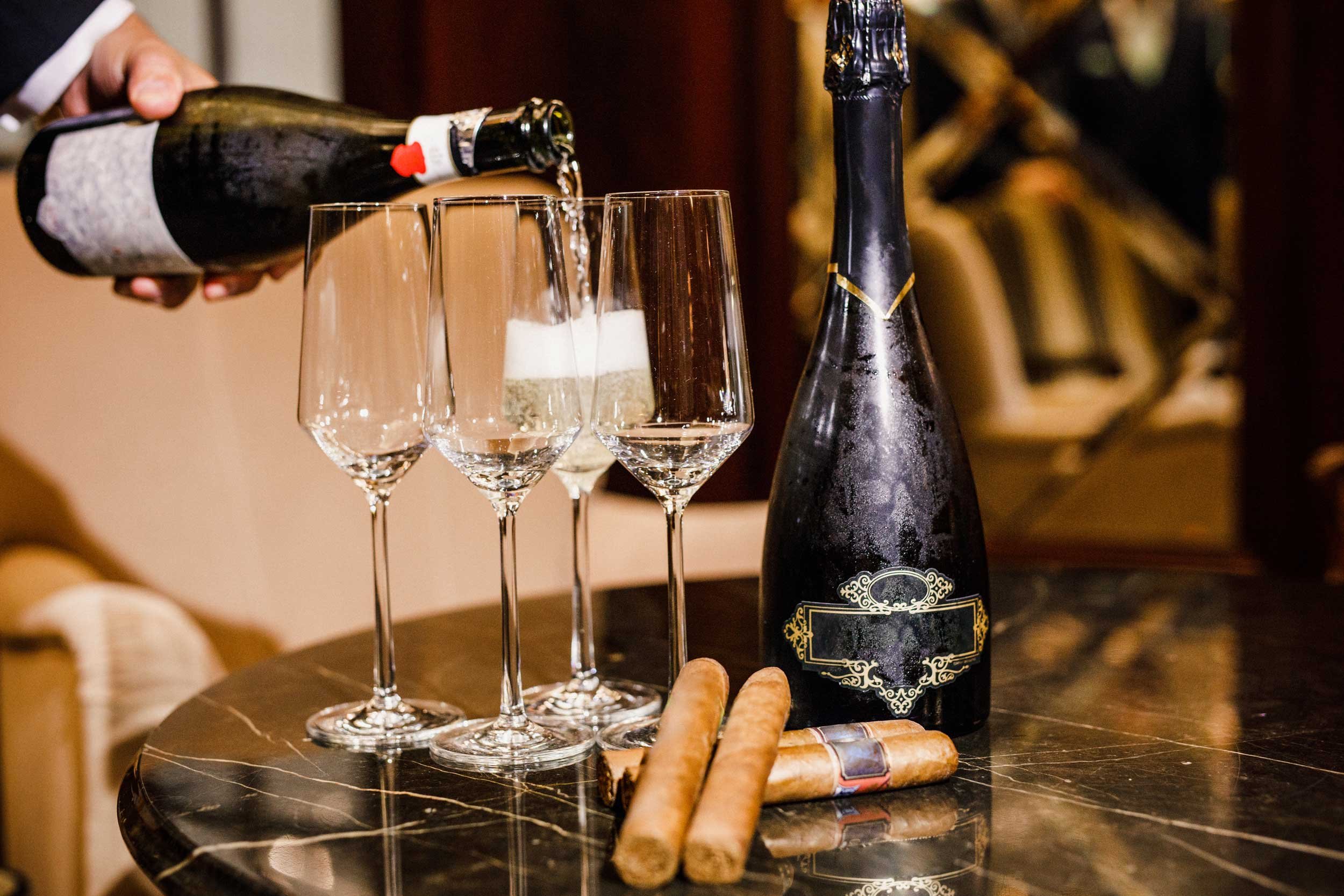 Sparkling wine poured into flutes beside cigars on dark marble.