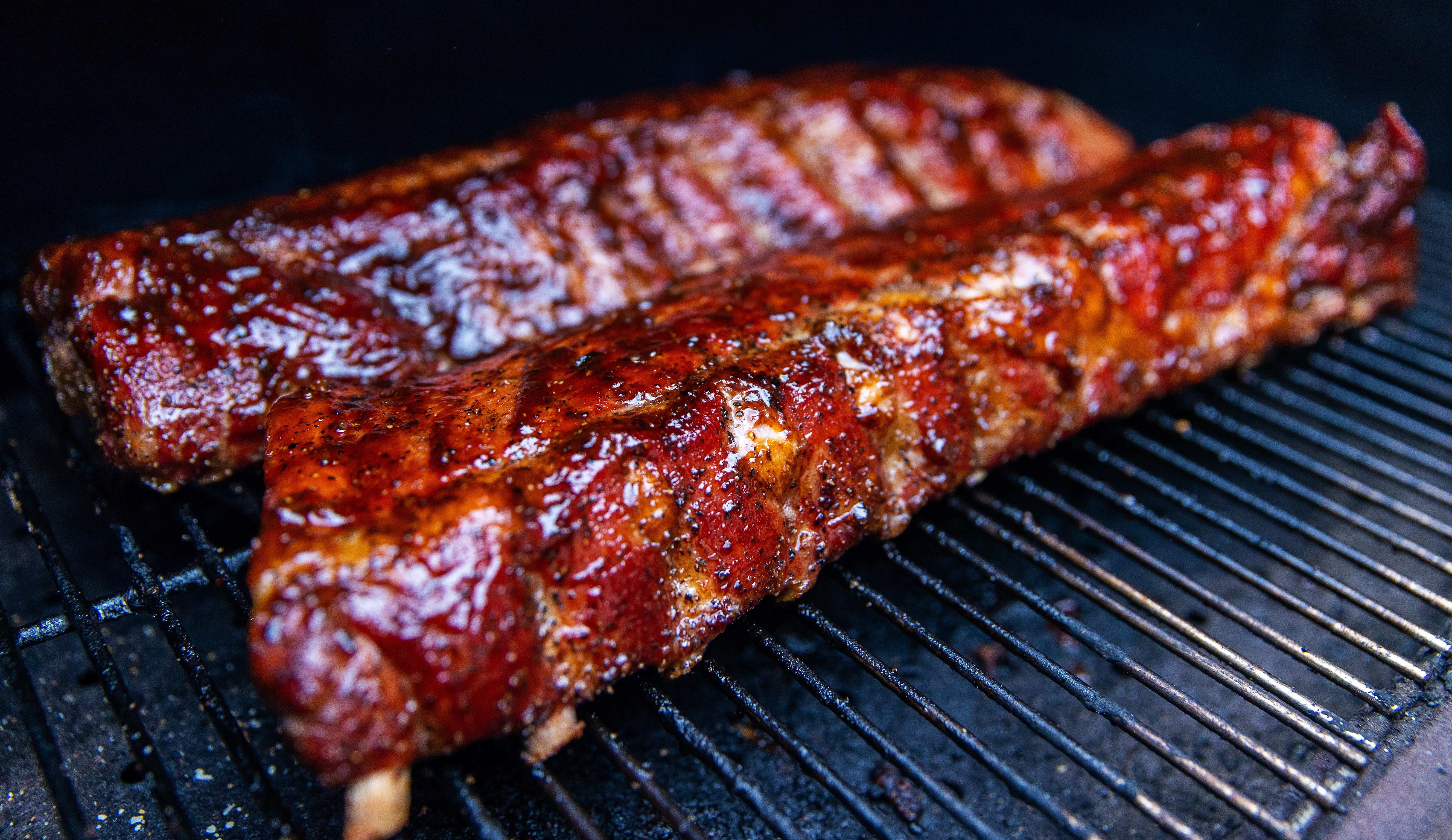 Baby-back pork ribs cooking on a pellet smoker, bark forming.
