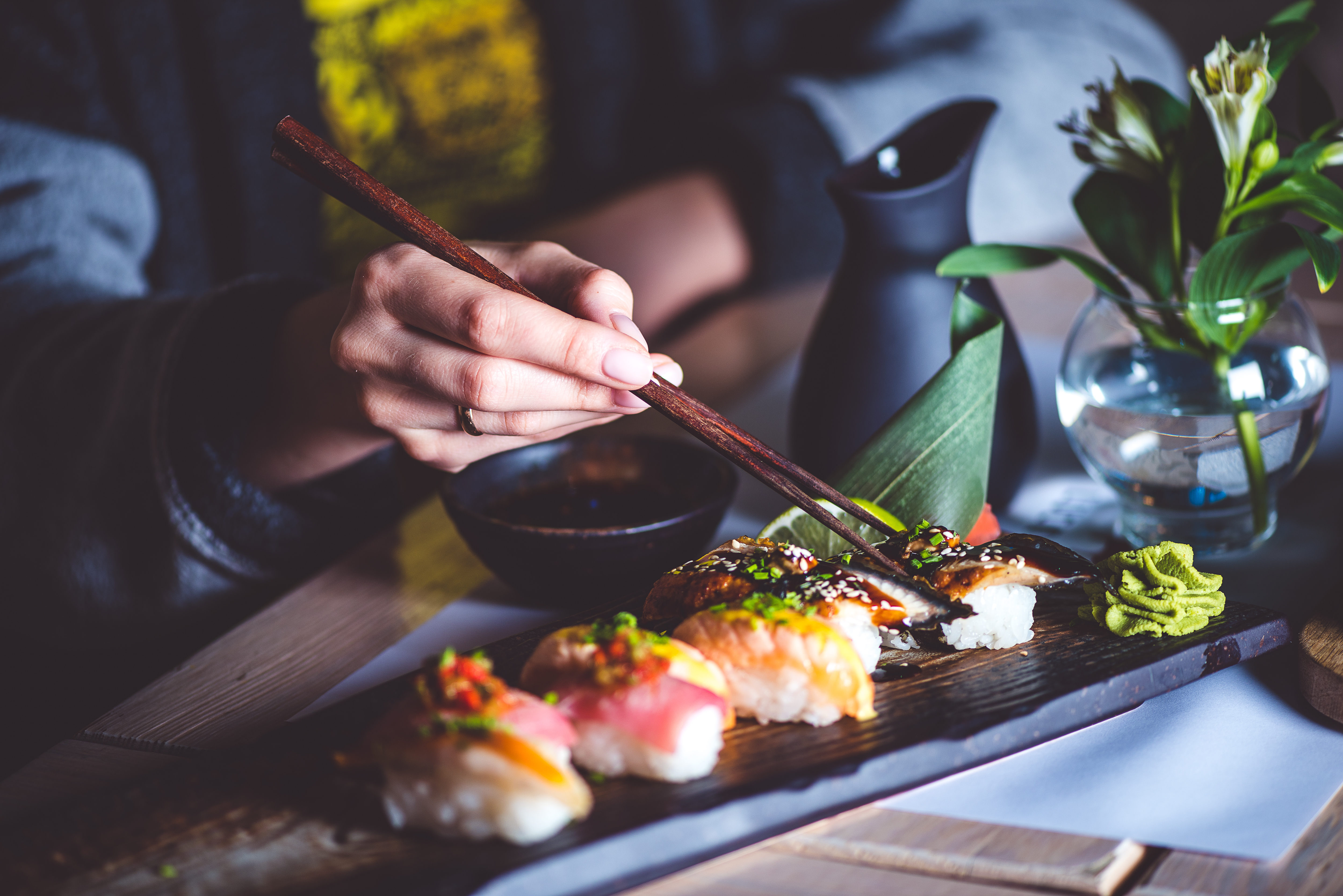 Chopsticks lifting unagi nigiri from a wooden board of salmon and white-fish nigiri.