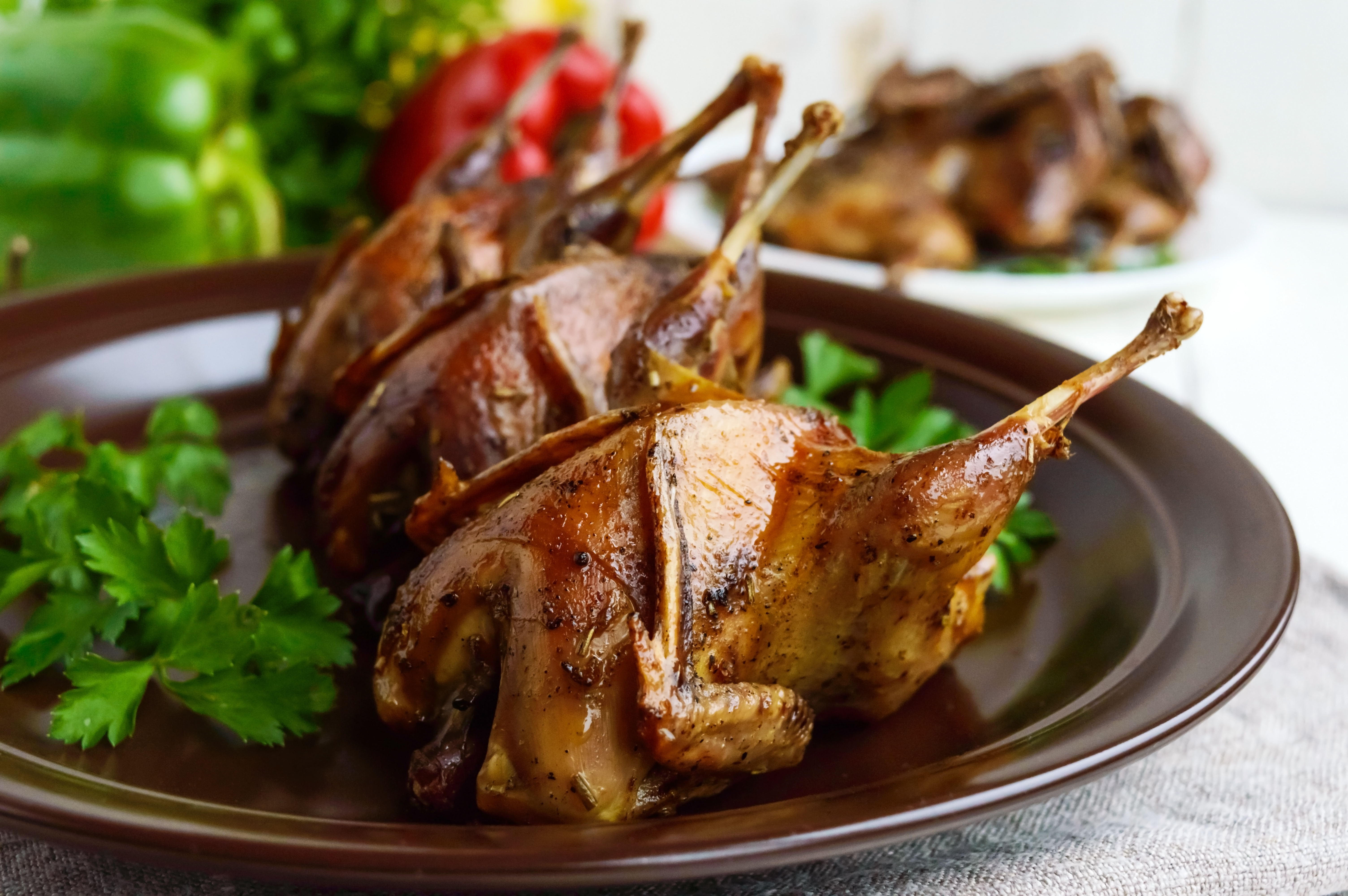 Four roasted quail on a dark ceramic plate with parsley.