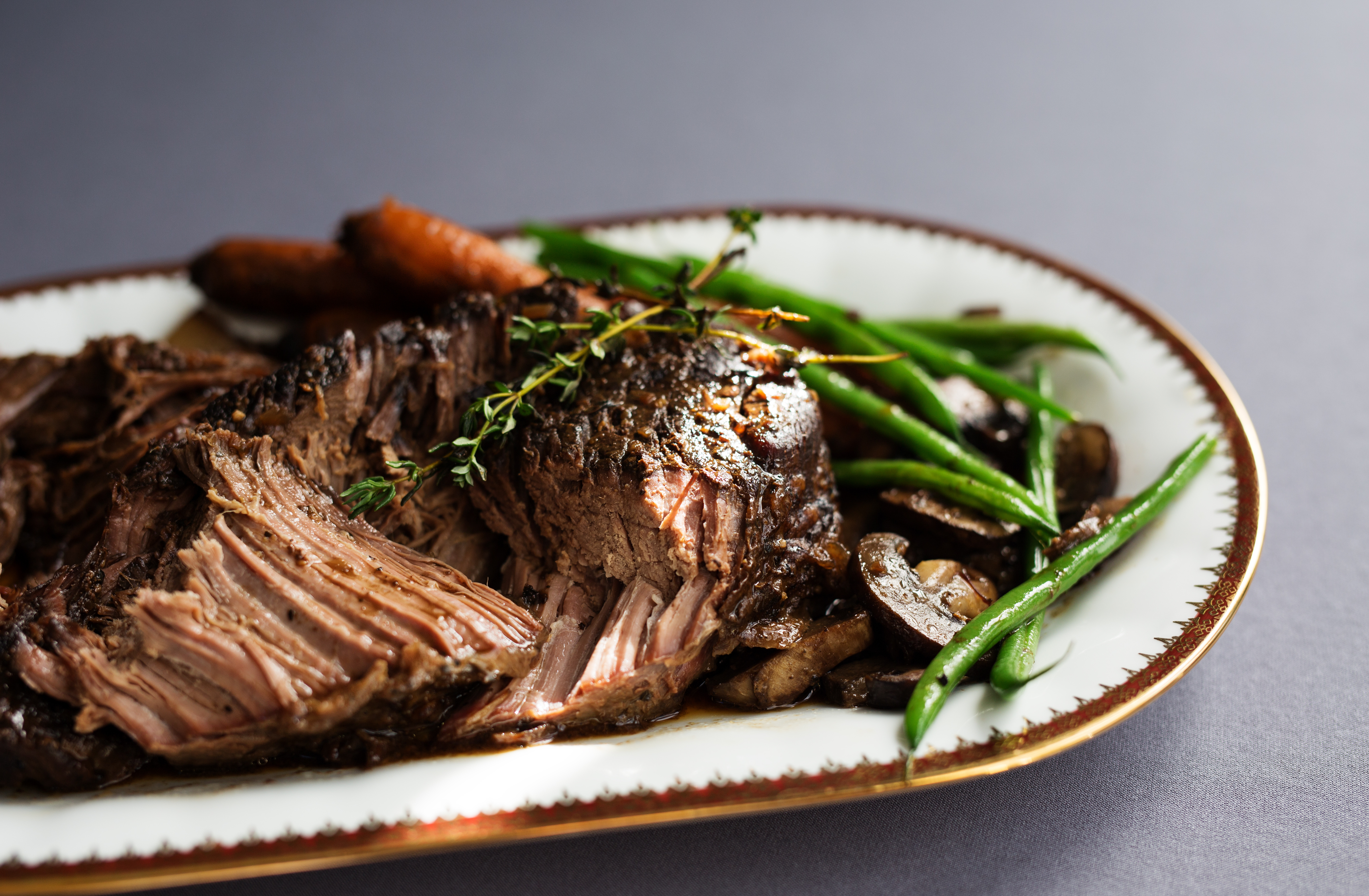 A plated beef roast with carrots, green beans, mushrooms, and thyme.