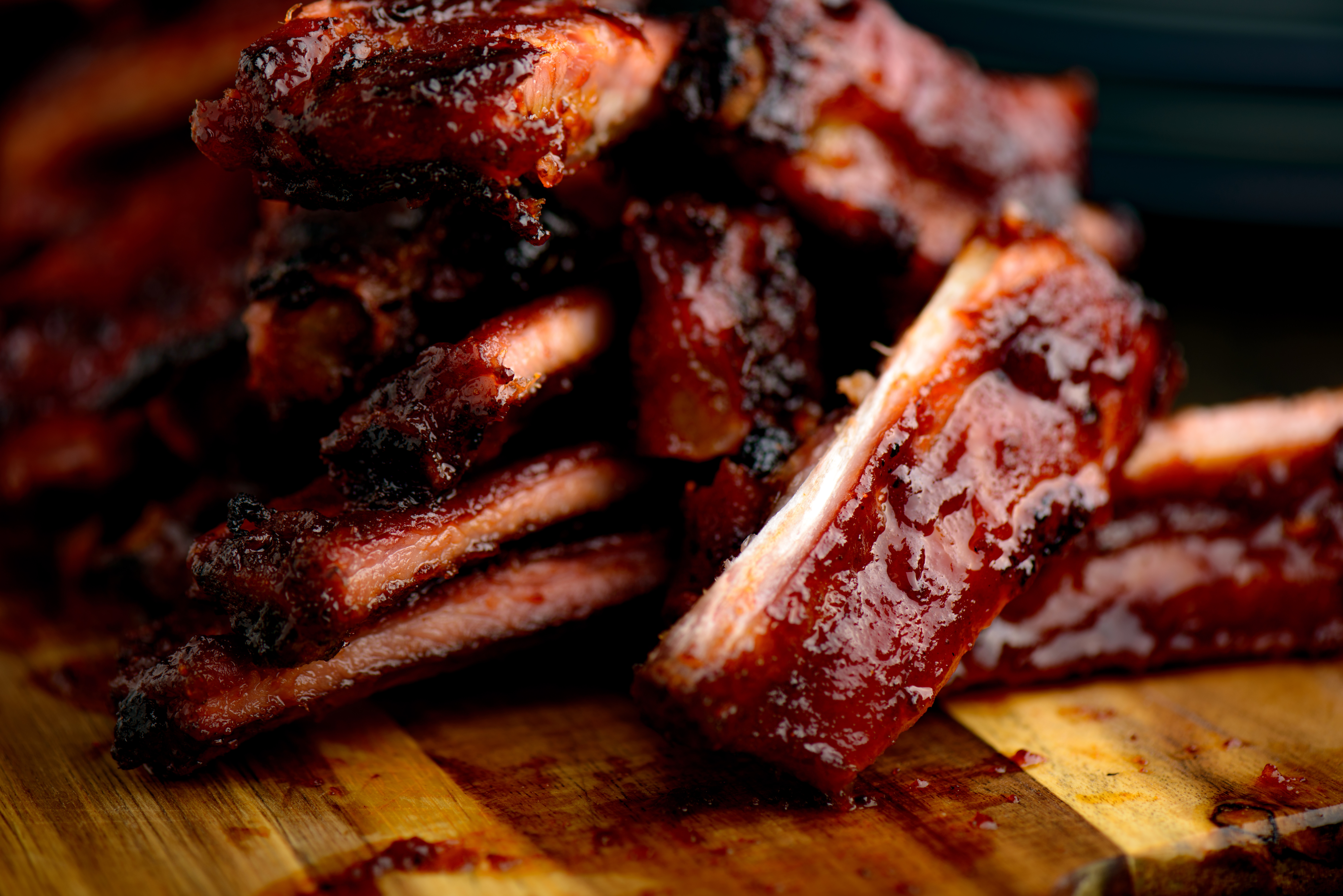 A rack of smoked ribs on a wooden plate, bark dark and sliced.