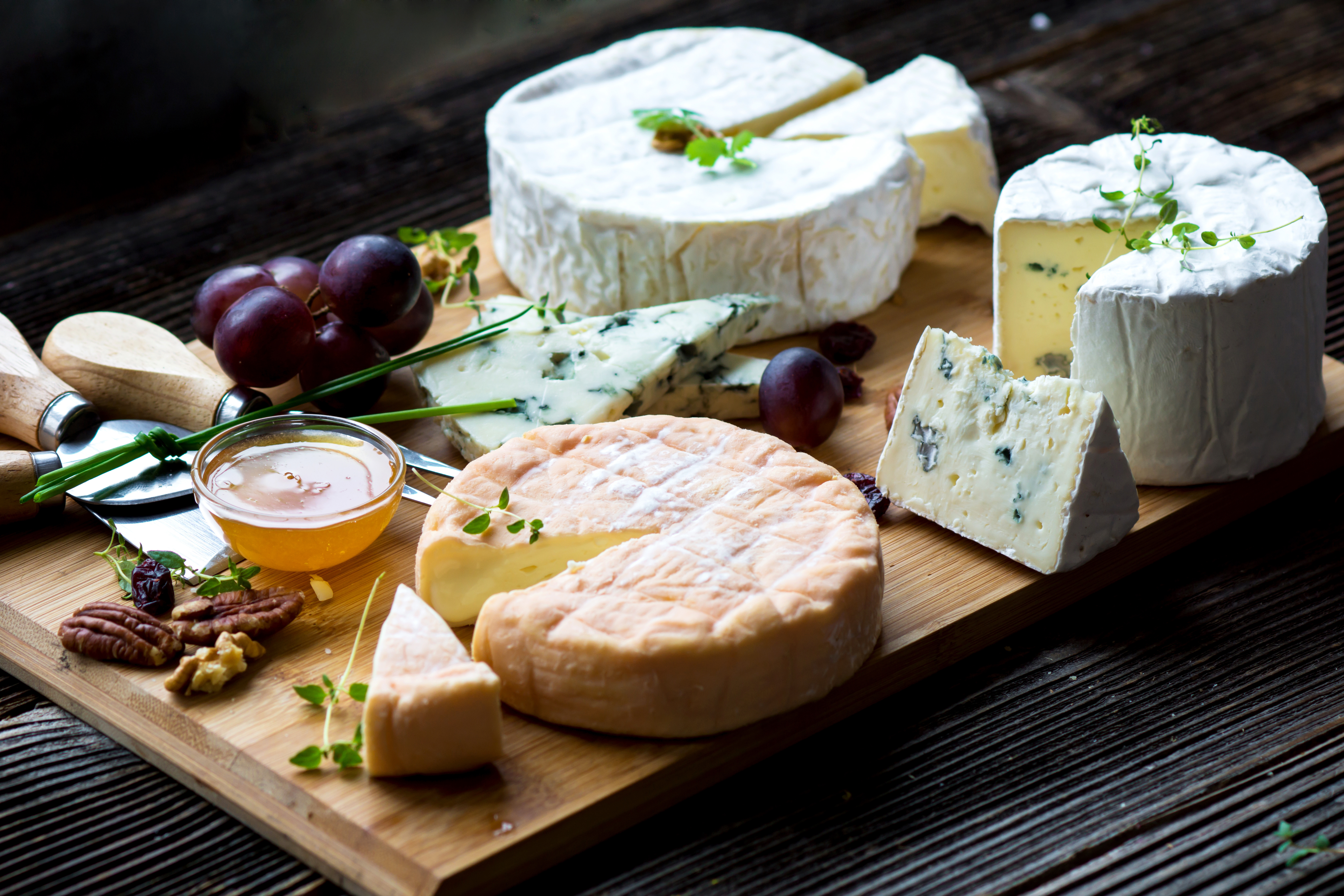 Washed-rind and blue cheeses with honey, grapes, and walnuts on a wooden board.